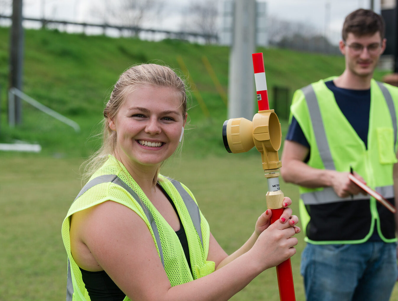 Civil engineering student smiling outdoors with surveying equipment