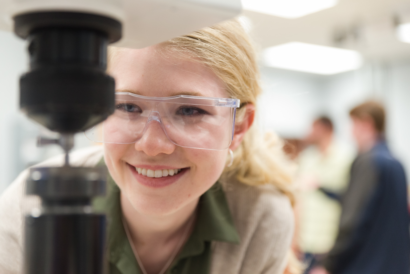 Mercer University female engineering student close-up in engineering lab, wearing protective goggles looking at machine and smiling