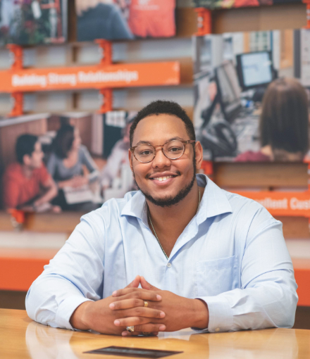 man sits with hands folded while smiling at the camera