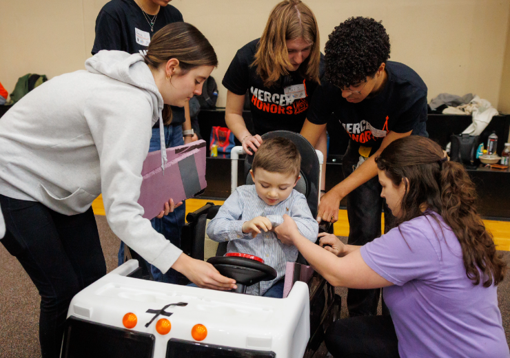 students work on a toy car while a child sits in the car